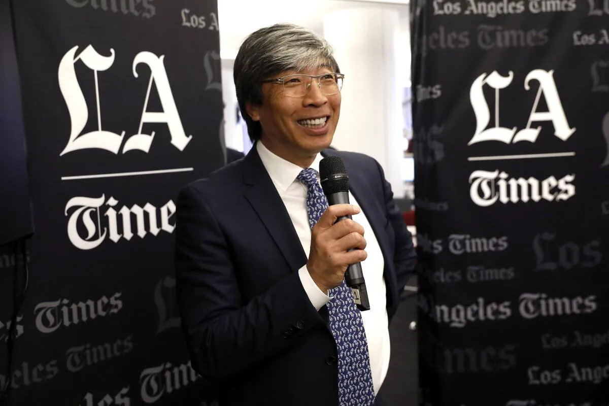 A man wearing a suit and tie is speaking into a microphone.