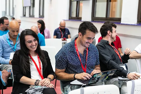 Attendees smiling and working on a laptop during a presentation.